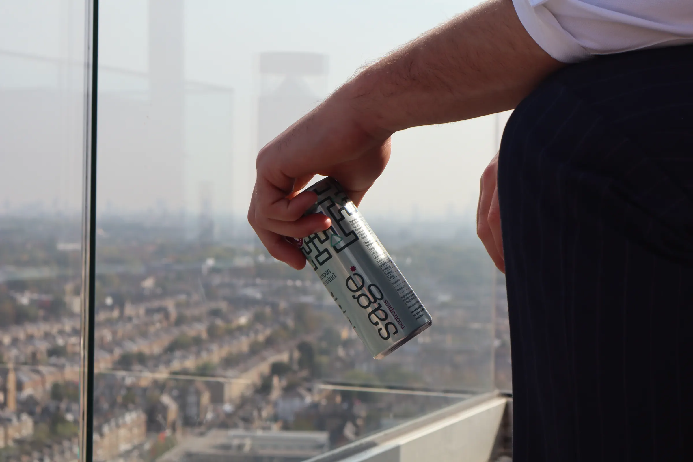 A can of sage held over a glass balcony with the city below