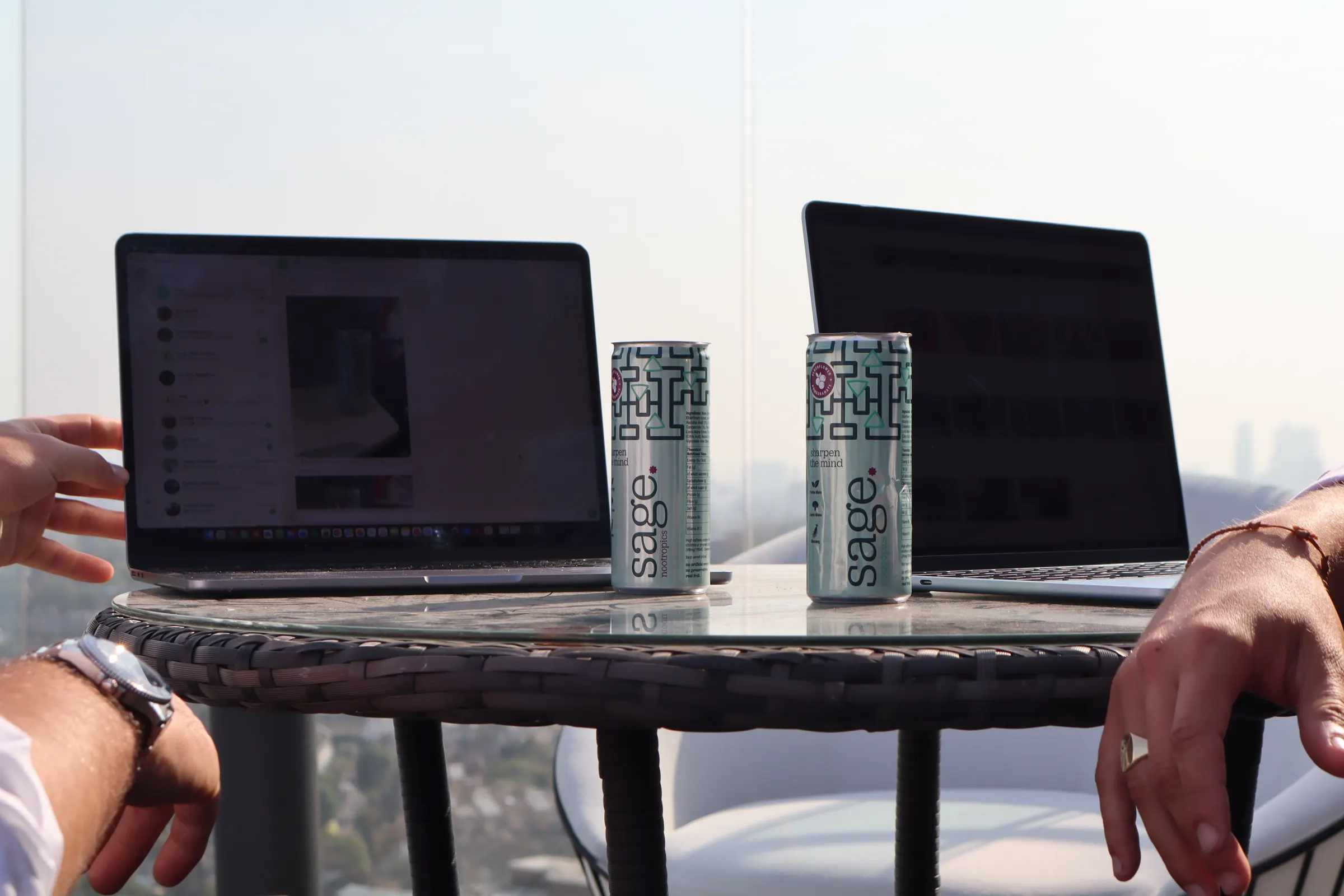 Two cans of sage on a table between two laptops