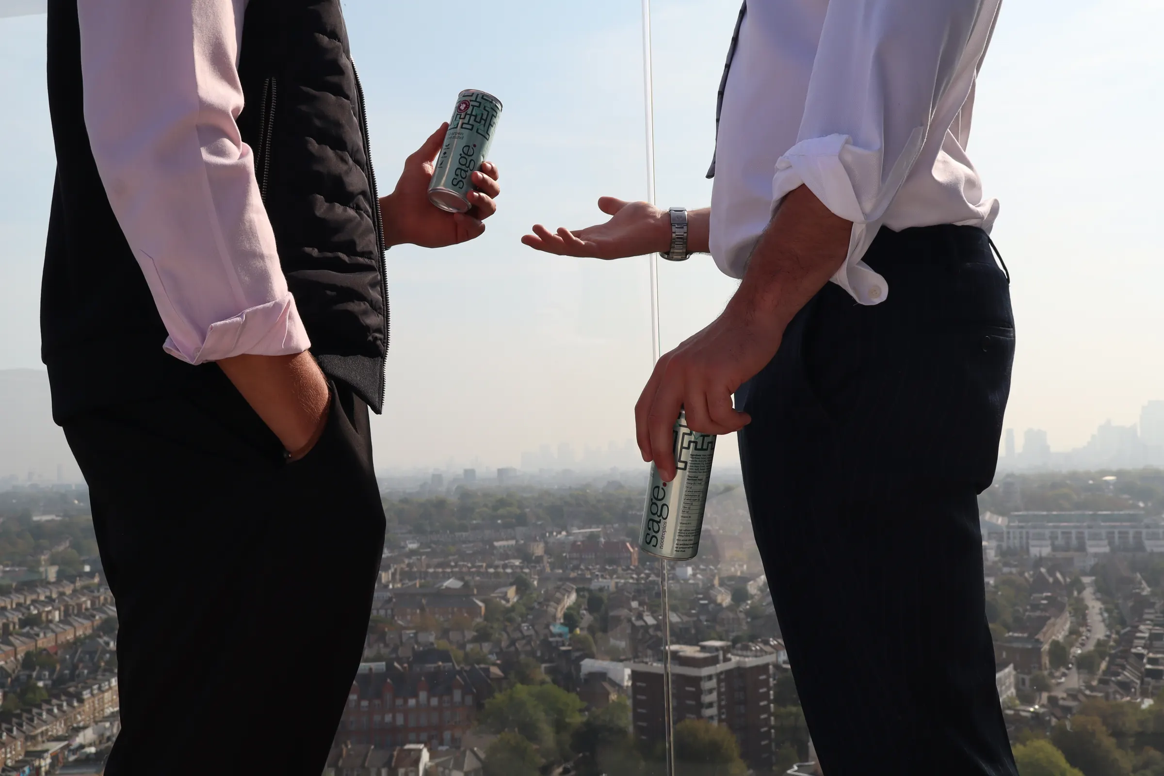 Two people talking on a London rooftop terrace, cans of sage in hand